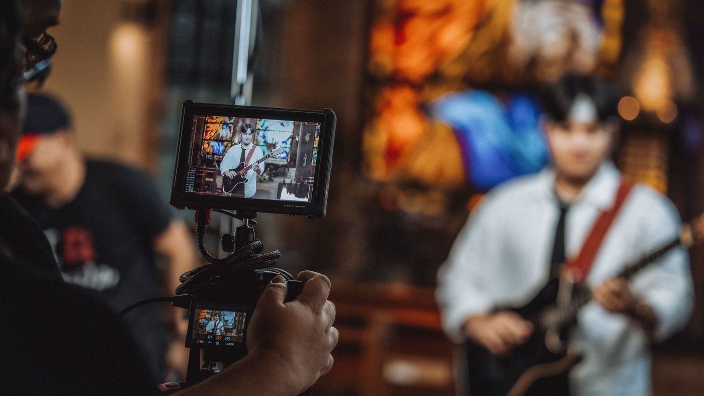 Close-up shot of hands holding a camera recording a guitarist during a live performance.