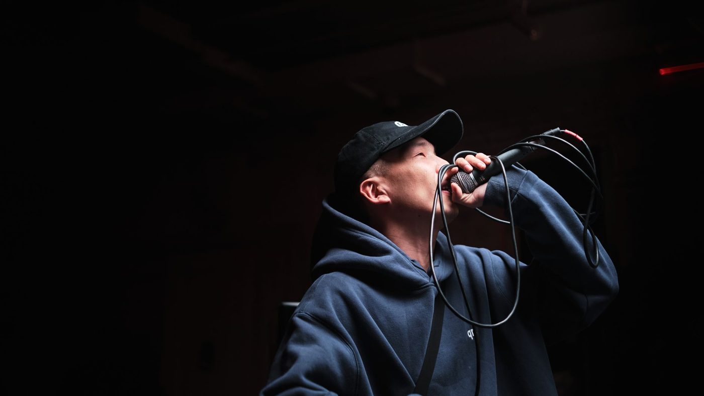 Dynamic shot of a male singer wearing a hoodie and cap, performing at a live concert with a microphone.