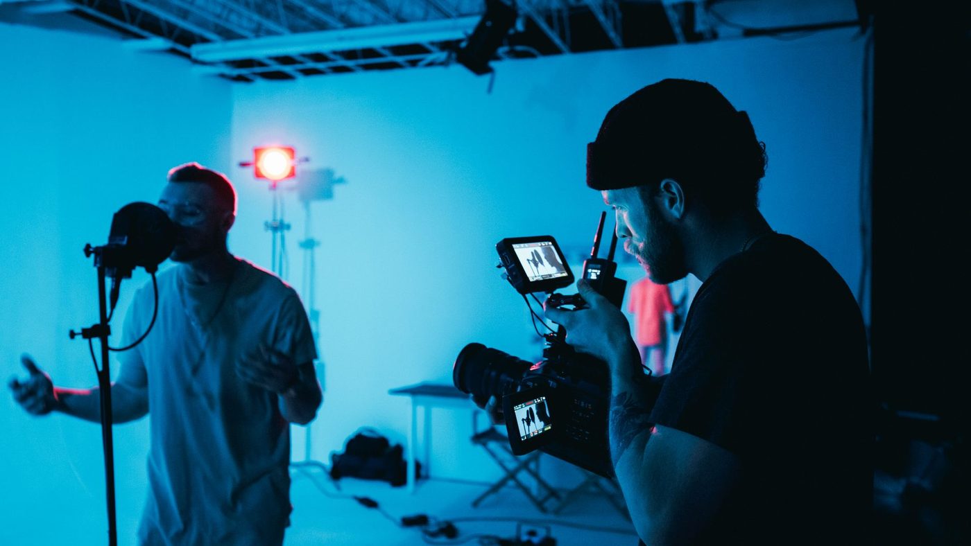 Male musician sings while videographer films in a studio setting.