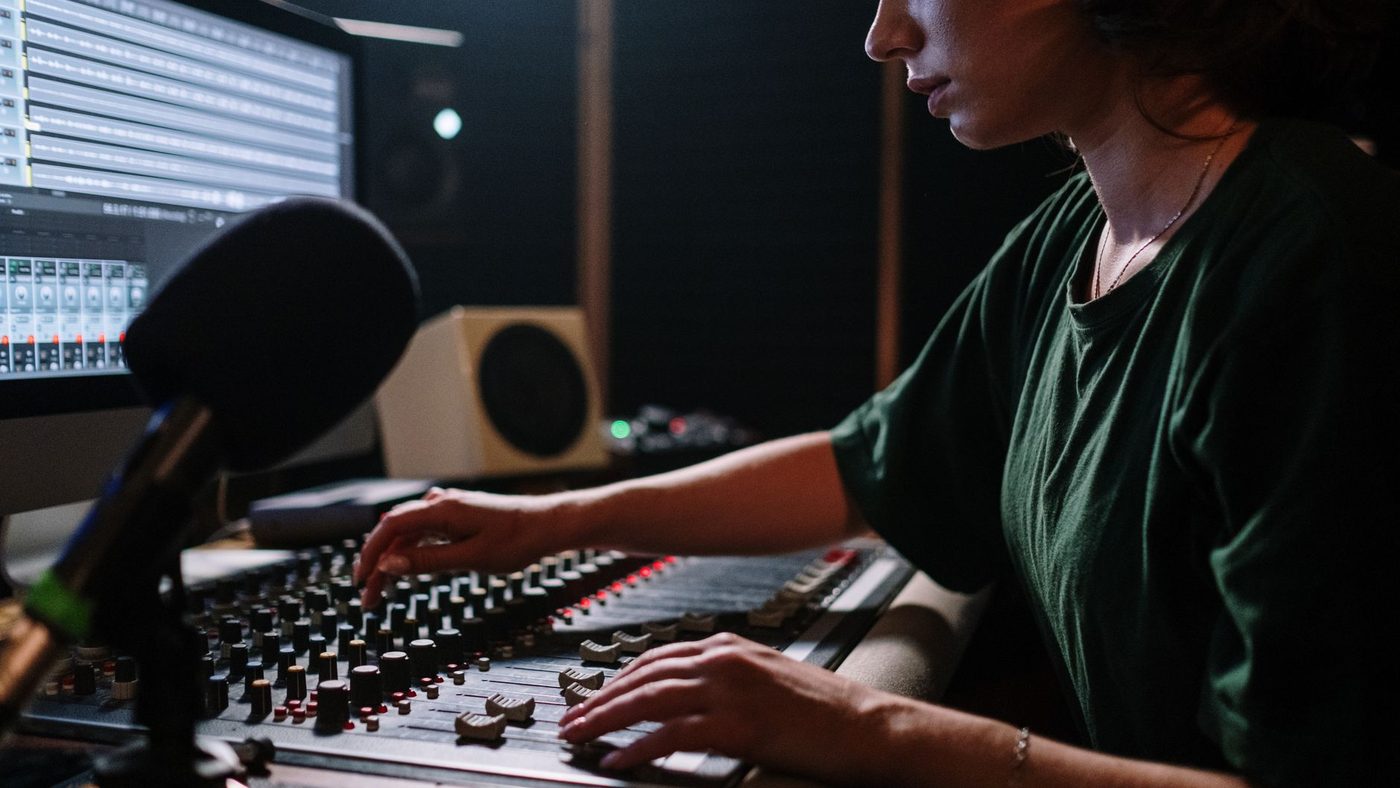 Focused woman operates a sound mixer in a music studio, enhancing audio quality.
