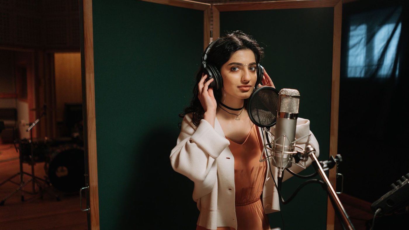 A female musician recording vocals in a professional music studio.