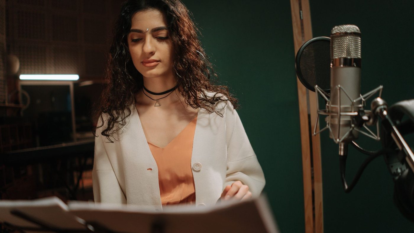 Professional female musician recording a song in a studio setting with microphone.