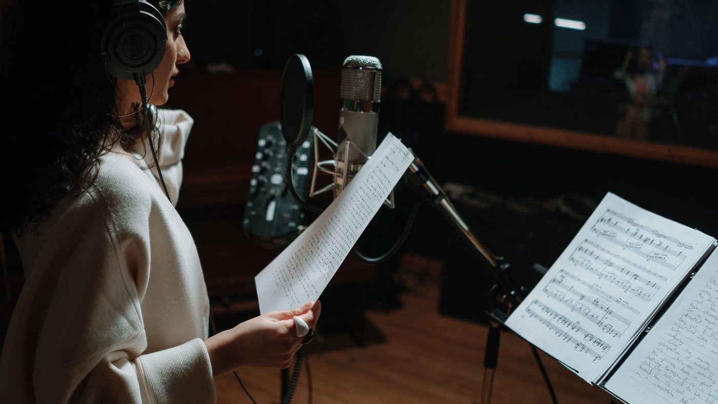 Woman in a music studio recording a song with a condenser microphone and headphones.