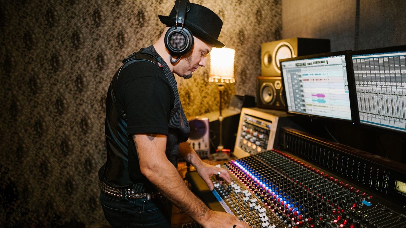 A music producer wearing headphones working at a mixing console in a cozy recording studio.