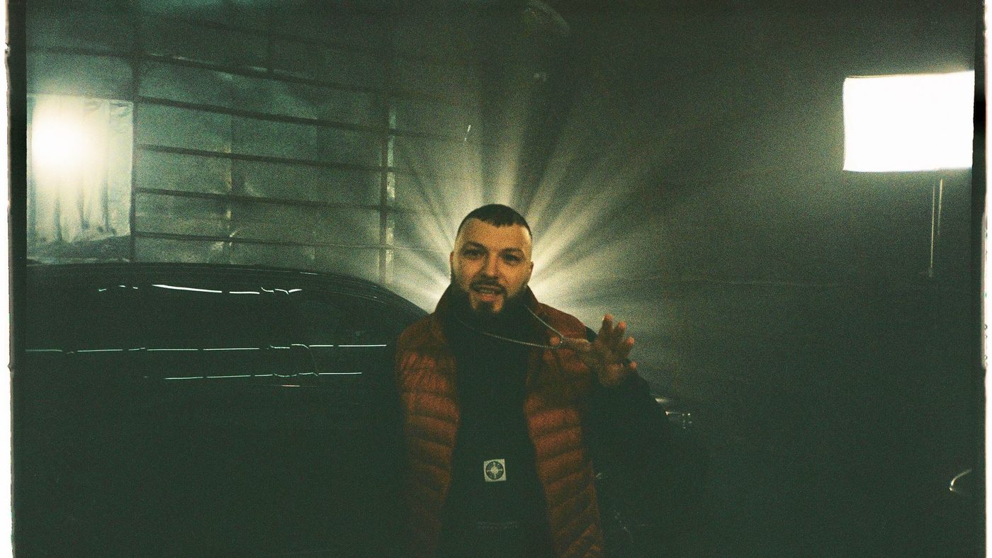 A musician in a red vest poses in dramatic lighting, showcasing style and confidence.